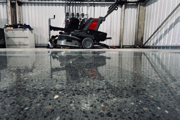 Finished polished concrete floor in a commercial workshop with grinding equipment in the background